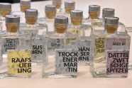 Viele Glasflaschen gefüllt mit Destillaten unterschiedlicher Sorten mit verschiedenen Etiketten nebeneinander auf einem Tisch