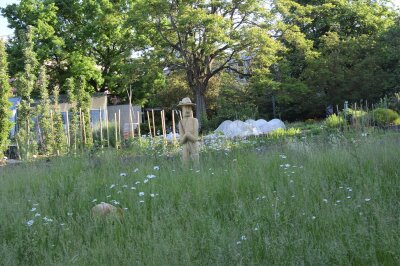 Holzfigur steht in einer Wiese mit Gräsern und Blumen