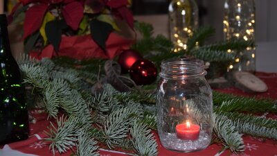 Weihnachtliche Dekoration mit Nadelzweig, Glas mit roter Kerze