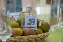 Eine Glasflasche gefüllt mit dem Destillat der Hänserbirne in einem Korb voller reifer Birnen