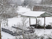 Verschneiter Garten mit Kisten und Dachunterstand.