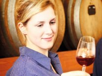 Eine junge Frau vor Holzfässern blickt in ein Glas mit Rotwein
