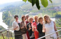 Sieben fröhliche Frauen mit Weinglas auf einem Balkon über Reben, Blick über Main und Land